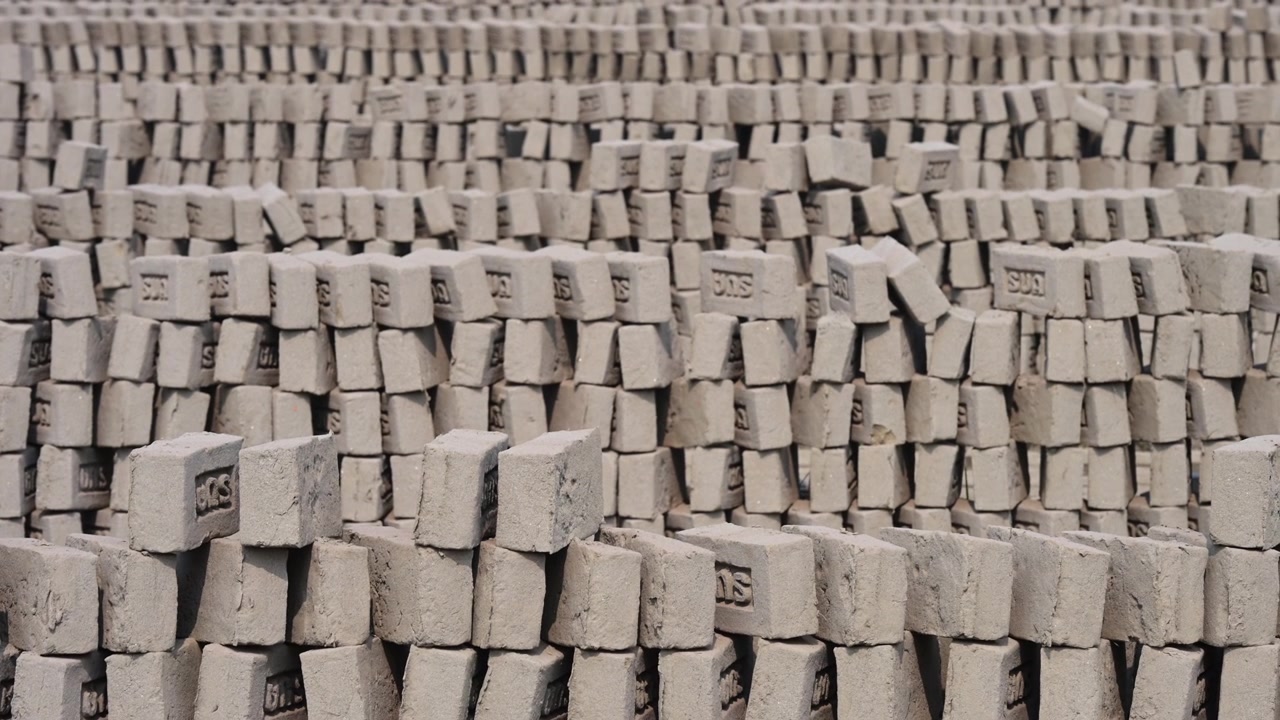 Uendelige stablede søjler af lerblokke, der hærder i solen på en fabrik i udkanten af Dhaka. Illustrerer massiv produktion af byggematerialer, traditionel fremstilling og regional handel.