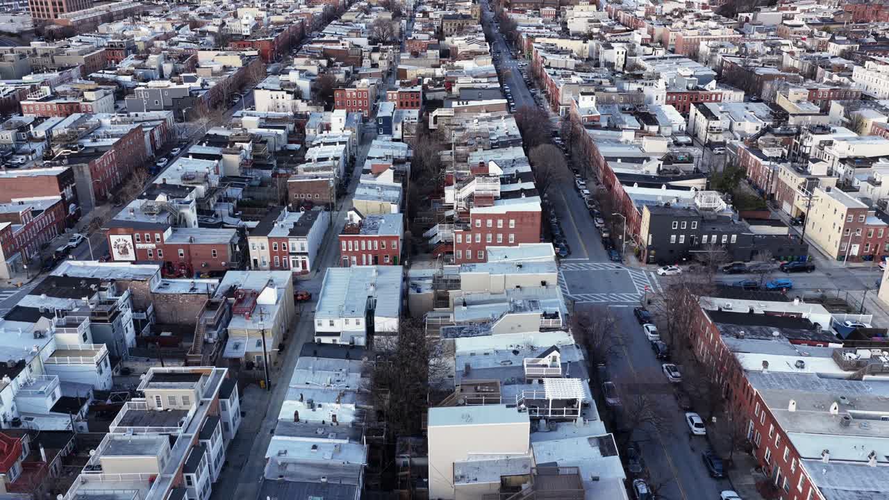 Volo di drone su un quartiere residenziale di Baltimora in inverno, che mostra strade residenziali diritte, case a schiera in mattoni e un layout urbano sotto una luce soffusa del tramonto. Inquadratura aerea. Tranquillo quartiere suburbano degli USA.