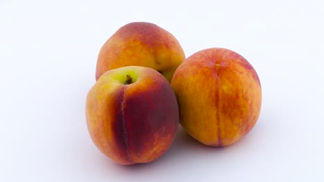 three peach fruits. rotating on the turntable. isolated on the white background. close up.