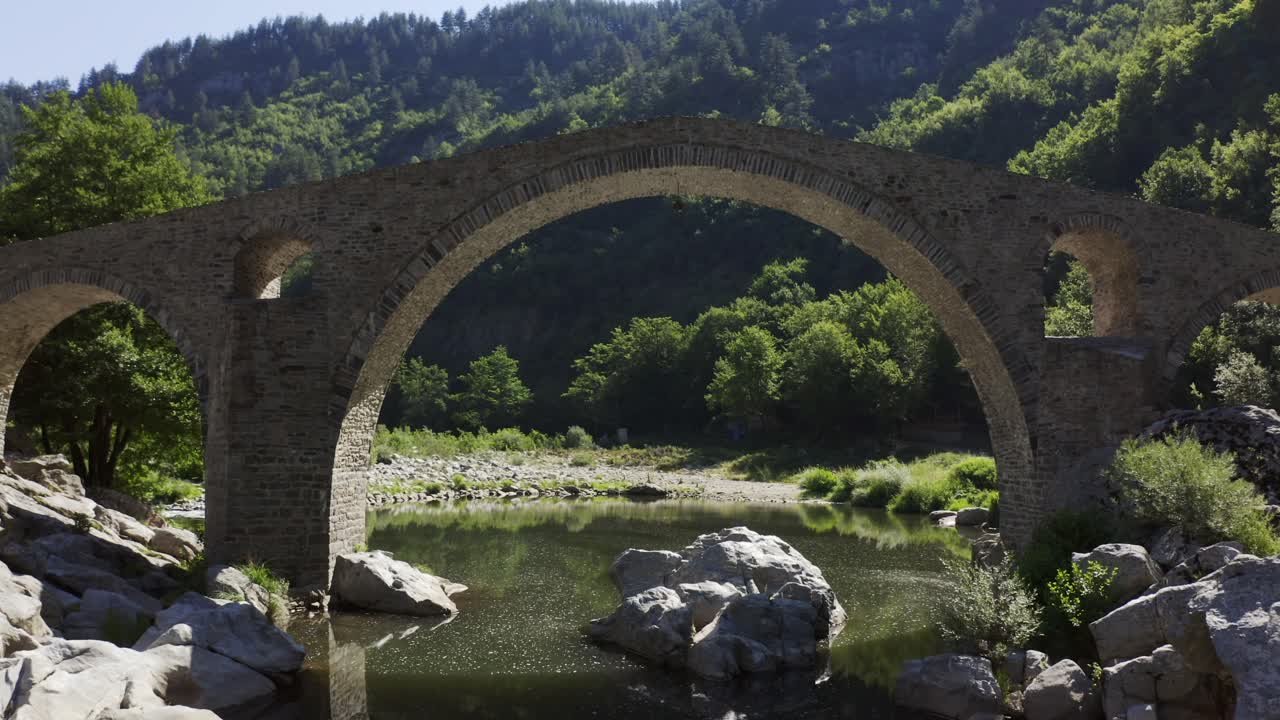 Approaching drone shot passing through the main arch of the Devil's Bridge over the Arda River located in the town of Ardino near the Rhodope Mountains in Bulgaria