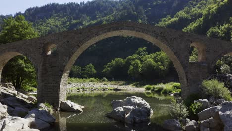 approaching drone shot passing through the main arch of the devil's bridge over the arda river located in the town of ardino near the rhodope mountains in bulgaria