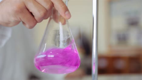 científico que mezcla valorante y analito en un matraz erlenmeyer agitando en un movimiento orbital - procedimiento de valoración en el laboratorio - primer plano