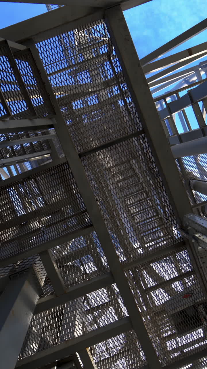 Steel frame construction on a factory. Modern storehouse construction. Metal structures of stairs rising up. Industrial plant. Vertical video