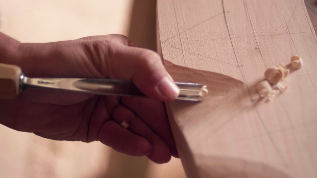 Woodworker's hand using a sharp metal tool to peel away thin shavings from a wooden block, focusing on texture and action. Slow motion close up