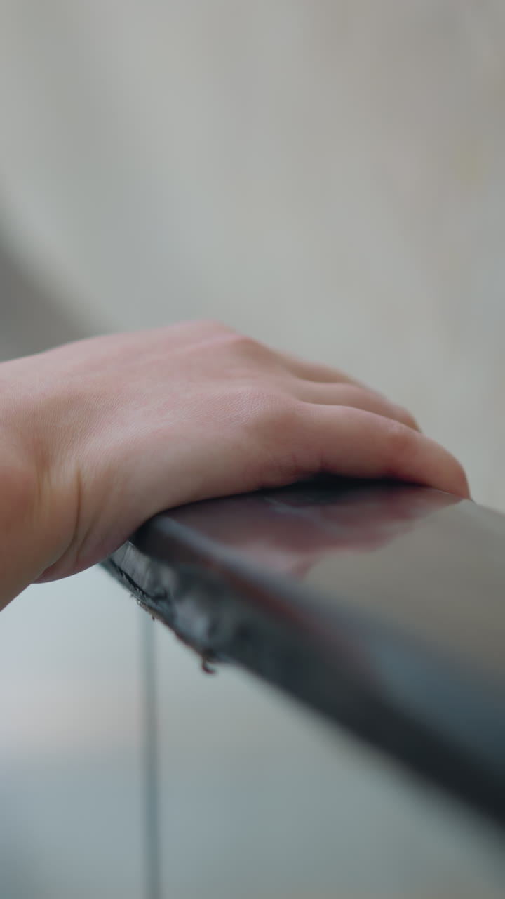 여성의 오른손이 에스컬레이터 레일에 누워있는 클로즈업, 부드러운 피부와 자연 손이 보이고, 현대적인 실내 환경에서 불분명한 인물이있는 흐릿한 배경