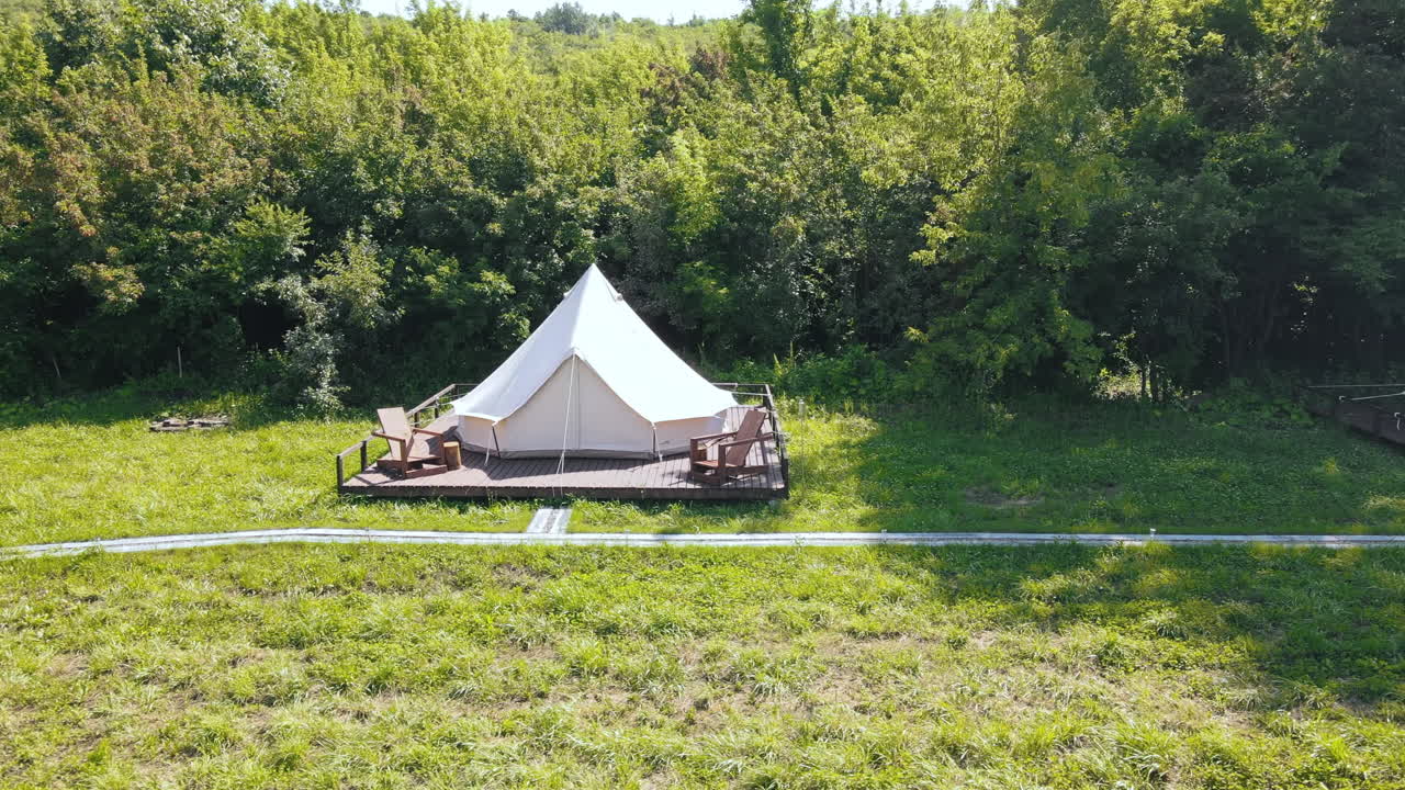 Glamping tents with chairs in the nature, green grass and trees, trail