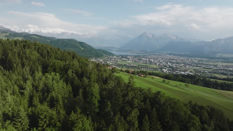 Aerial-of-a-forest-with-a-small-town-and-mountains-in-the-background