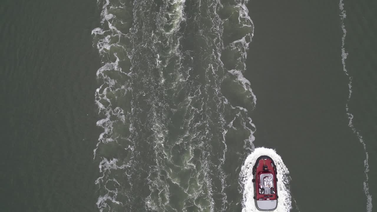 una vista de arriba hacia abajo sobre dos remolcadores que viajan por el río hudson en un día nublado siguiendo un contenedor