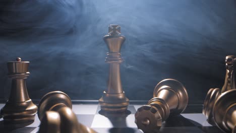 Dramatic-smoky-dolly-out-on-gold-king-with-fallen-pieces-around-on-chess-board