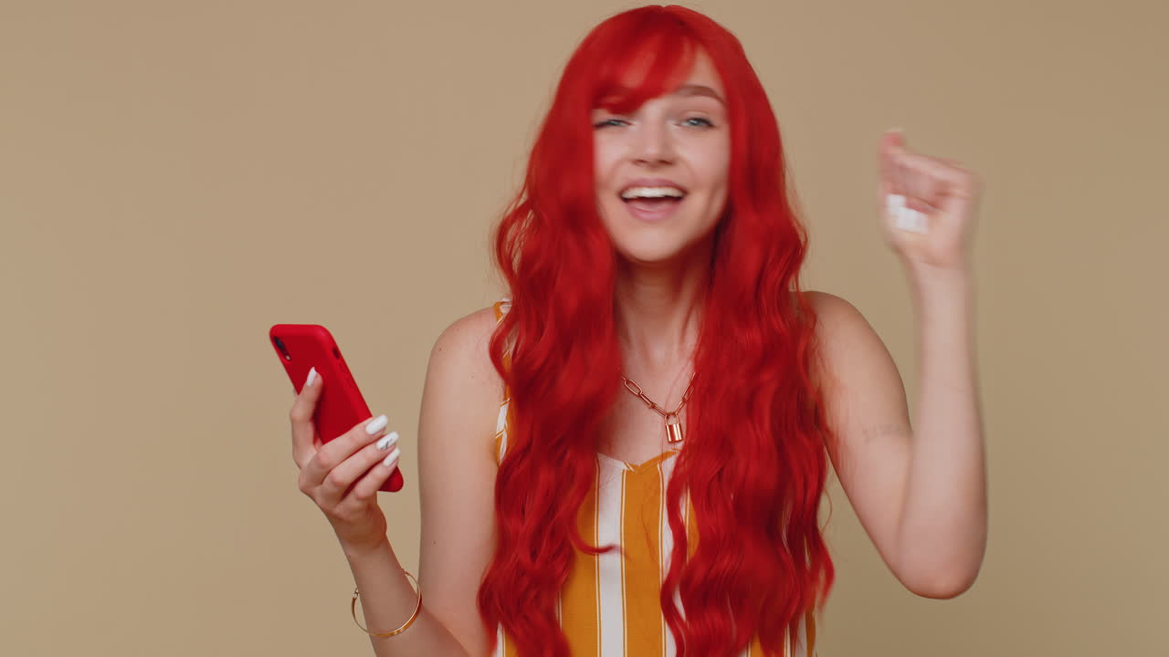 행복하고 흥분된 여자는 휴대폰을 사용합니다. 와우 예, 우승자 몸짓을 하면서 큰 승리 소식을 알아냈습니다.