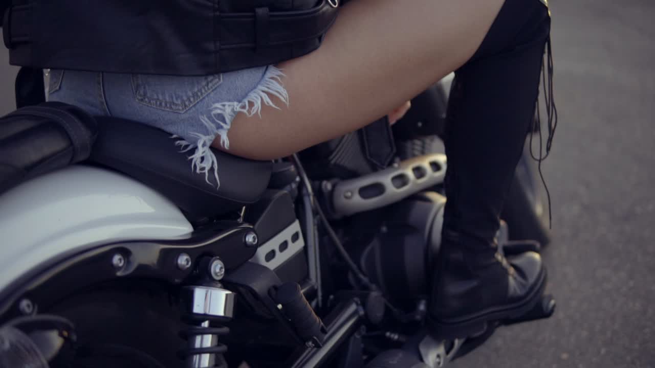 모터사이클 좌석에 앉아 긴 머리카락을 가진 여성 바이커의 뒷면. 그녀와 함께 헬리 ⁇ 터에 젊은 곱슬머리 여성의 클로즈업