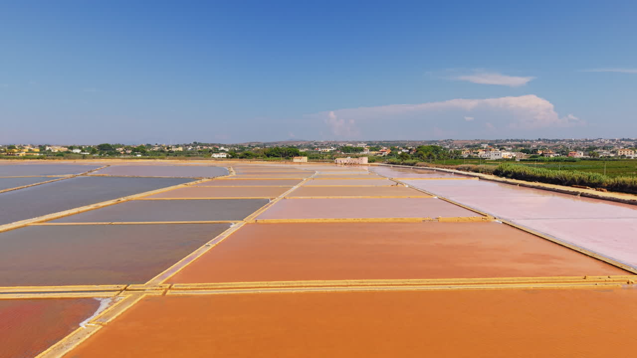 Aerial drone flight over colorful salt pans in Sicily, Italy, stunning natural patterns with orange, pink and blue water