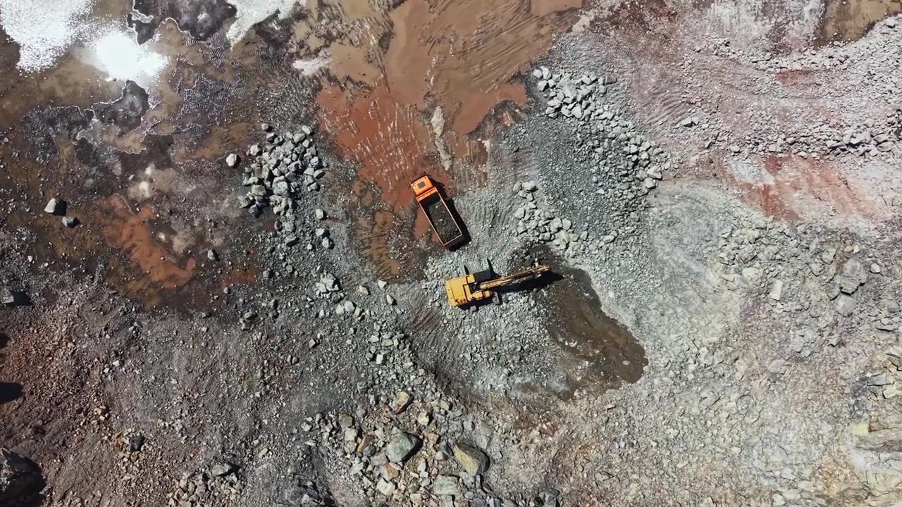 Granite quarry operation showing heavy machinery and rocky terrain during daylight hours with trucks and equipment moving materials