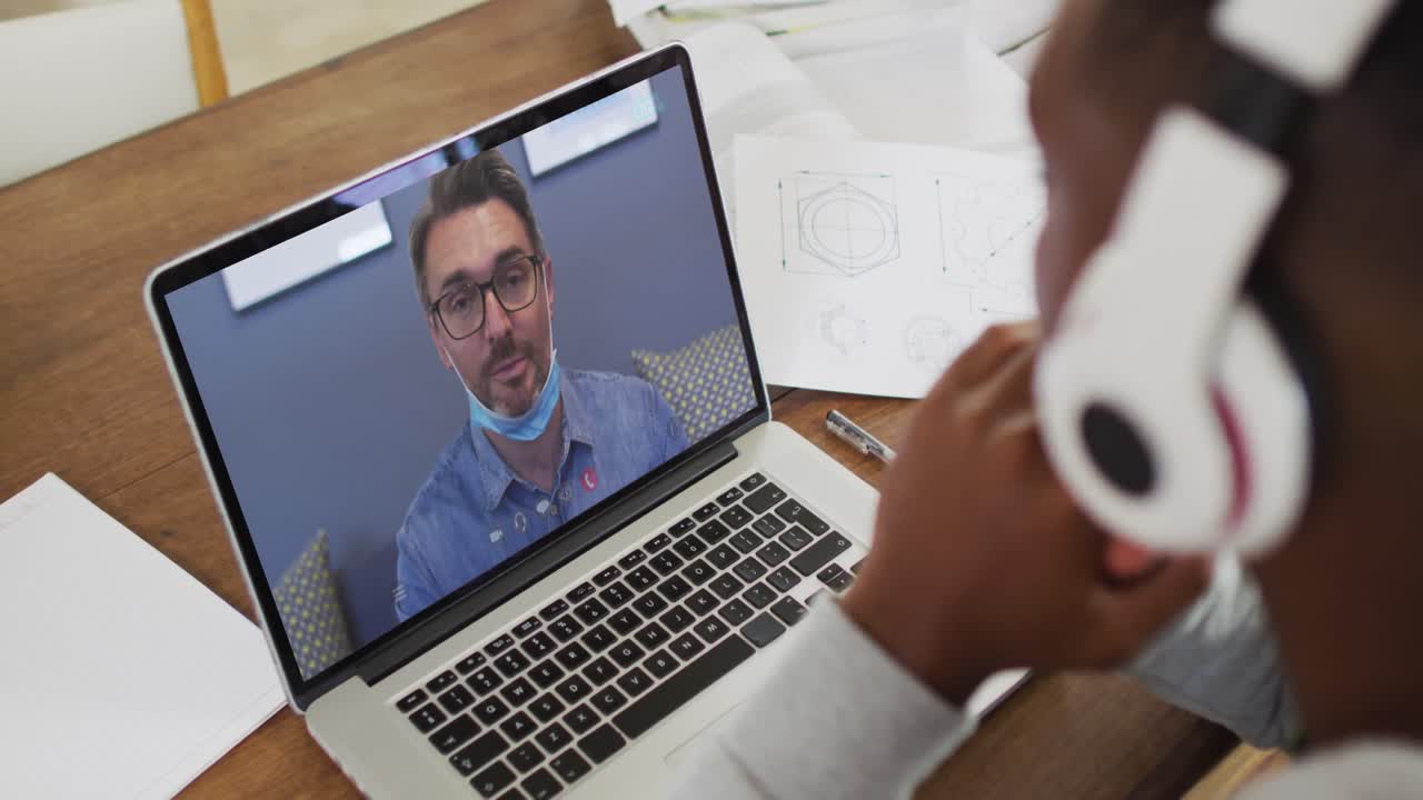 estudiante universitario afroamericano que usa auriculares haciendo una videollamada en una computadora portátil en casa