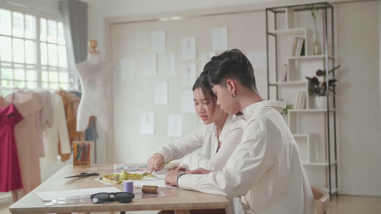 นักออกแบบแฟชั่นชาวเอเชียหนุ่มสาวสองคนกำลังร่างแบบที่สตูดิโอออกแบบแฟชั่น