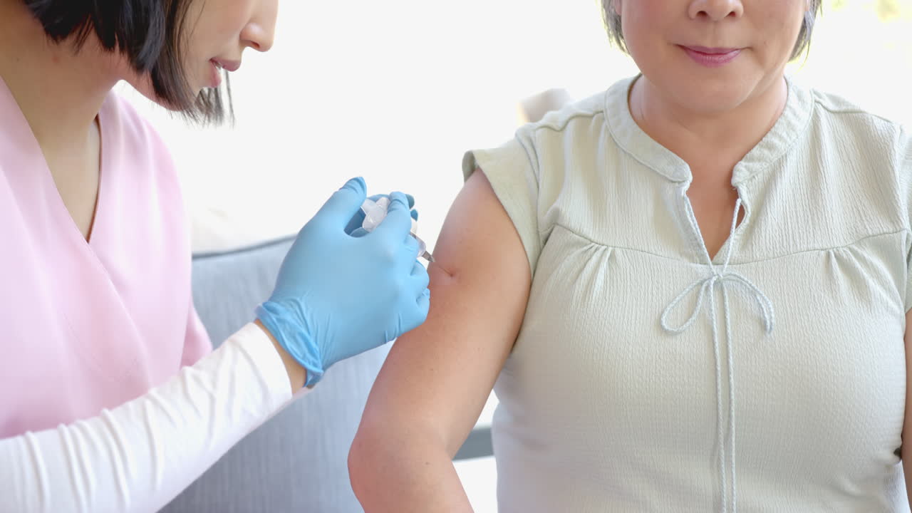 Administering vaccine, healthcare worker giving injection to senior asian woman at home