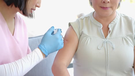 administering vaccine, healthcare worker giving injection to senior asian woman at home