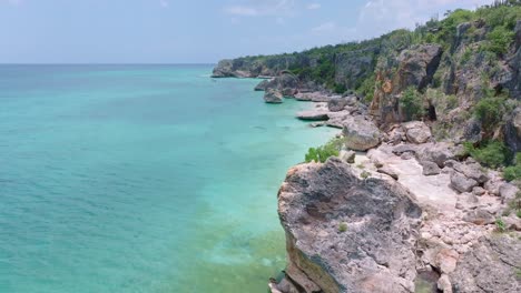 drone flying at low altitude over tropical waters sea along rocky cliff of jaragua national park, pedernales in dominican republic