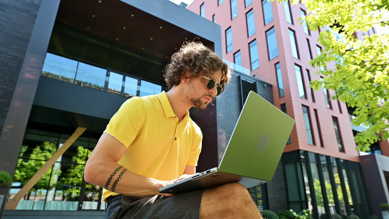 Man in yellow shirt talking standing on a bench and working on a laptop