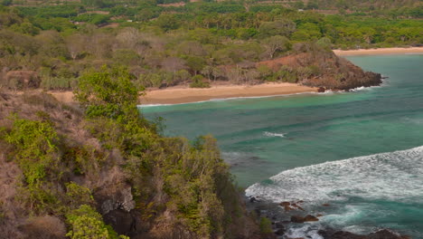 Aerial-view-of-lush-tropical-beach-with-mountain-backdrop,-Sumbawa-Island,-Indonesia