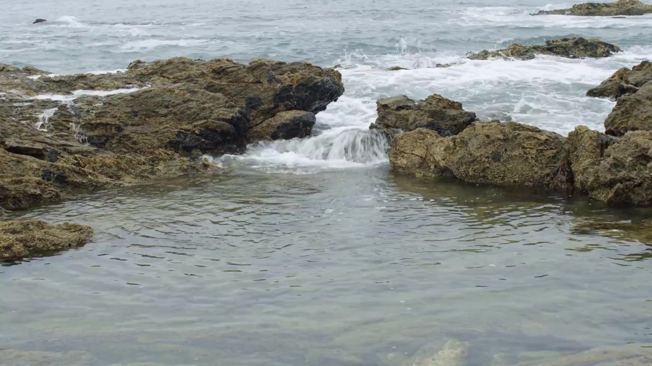 Acqua che si riversa. Pozza di marea rocciosa lungo la costa del Pacifico con potenti onde oceaniche che si infrangono sotto un cielo nuvoloso e cupo
