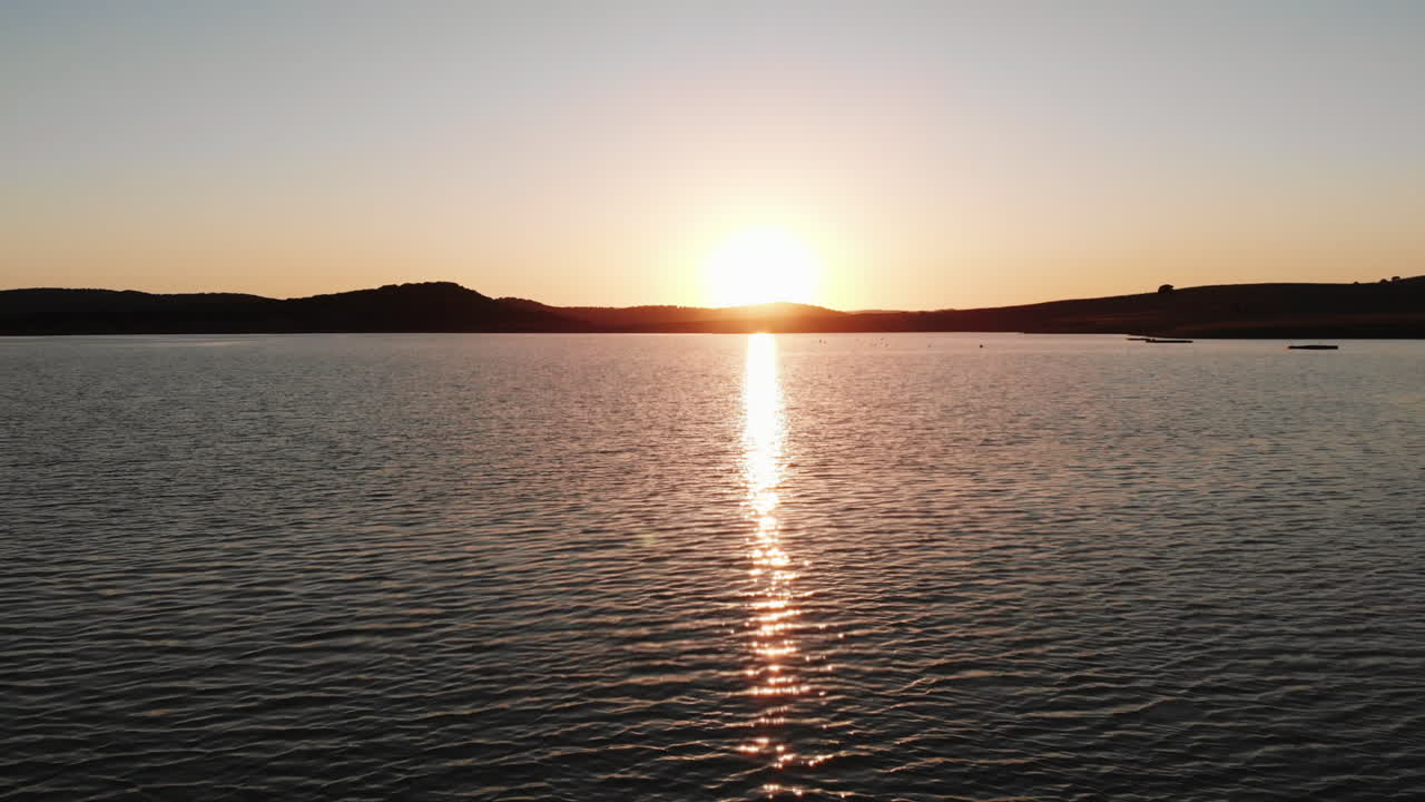 Golden sunset almost hiding behind the mountains on the horizon, lighting Wakana lake in Cádiz, Spain - Aerial Fly-over tilt up reveal