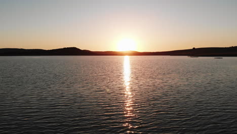 goldener sonnenuntergang, der sich fast hinter den bergen am horizont versteckt und den wakana-see in cádiz, spanien, beleuchtet - nach oben geneigter luftüberflug enthüllt