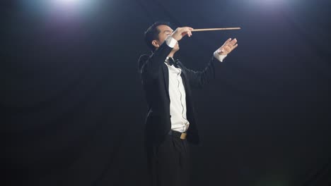 side view of asian conductor man holding a baton closing his eyes and showing gesture in the black studio