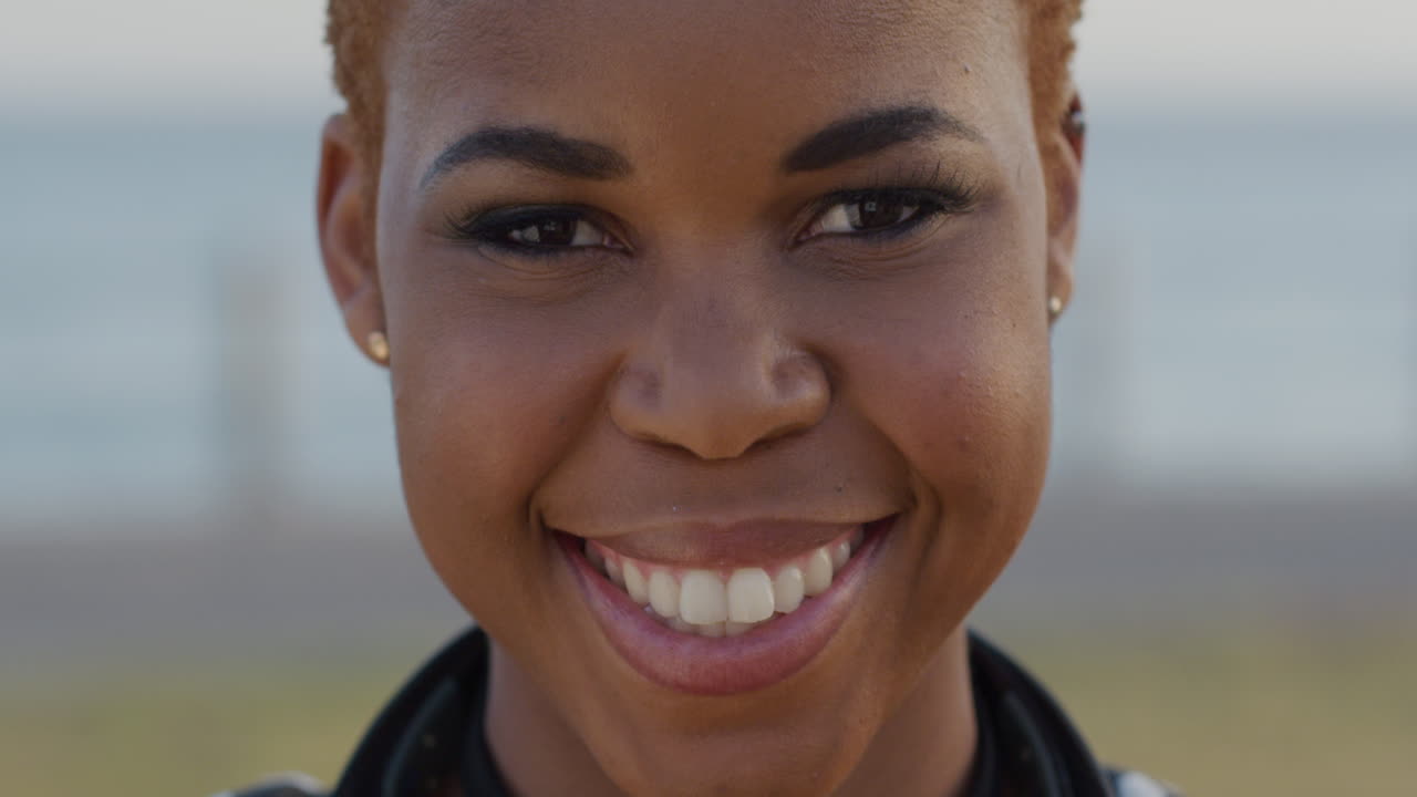 Retrato de jovem mulher afro-americana feliz sorrindo ao ar livre à beira-mar, desfrutando de um estilo de vida tranquilo