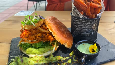 Juicy-pulled-chicken-burger-with-onion-rings,-avocado,-crispy-kale,-brioche-bun-and-sweet-potato-french-fries,-food-restaurant,-4K-shot