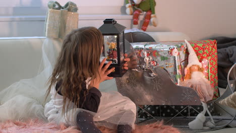 young adorable child looking at christmas snow globe with reindeer and falling snow