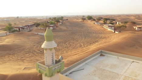 aerial view of an empty abandoned village and homes with a mosque covered in desert sand near dubai