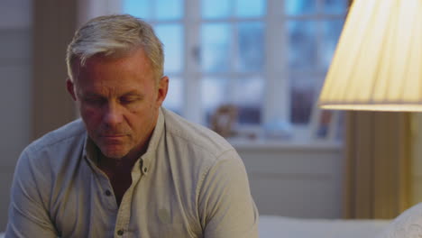 Depressed-mature-man-at-home-sitting-in-bedroom-in-evening-looking-sad--shot-in-slow-motion