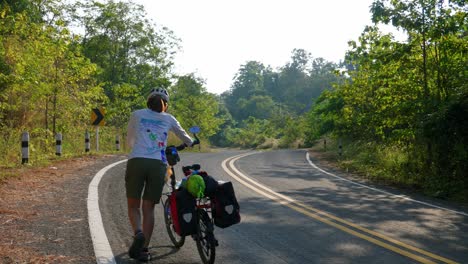 Rear-view-of-women-walking-with-cycle-in-the-forest-road-of-Pak-Nai-fisherman-village,-Nan-province,-Thailand