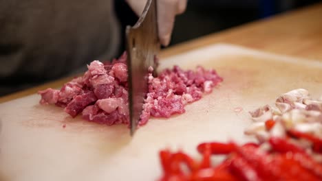 hand with glove chopping raw beef with pad kra paw ingredient on white chopping board, close up-2