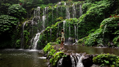 Female-influencer-stands-in-front-of-epic-falls-in-Bali-jungle-with-lush-foliage