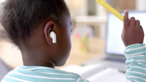 chica afroamericana con auriculares aprendiendo en línea en la mesa usando computadora portátil, cámara lenta