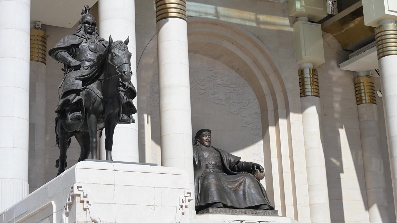 In una giornata di sole a Piazza Sukhbaatar, Ulaanbaatar, l'imponente statua in bronzo di Gengis Khan si erge al centro, affiancata da una statua di un soldato a cavallo di fronte al Palazzo del Governo