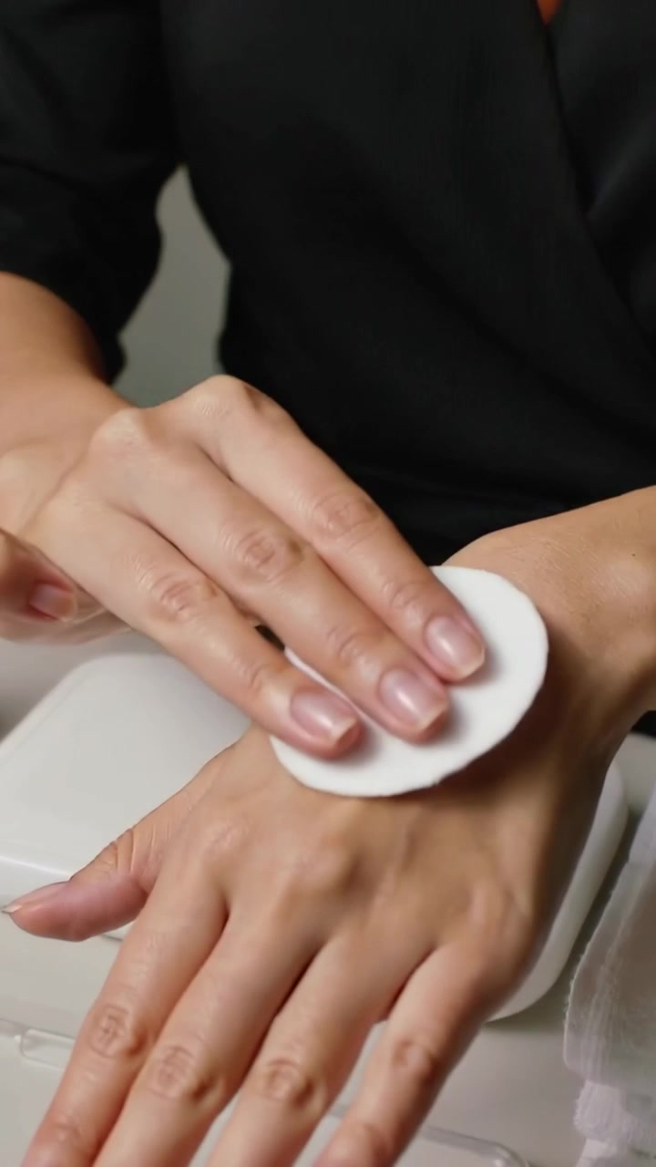 Vertical video: Dispensing on pad, woman in black top cleansing left hand at vanity with rose watch