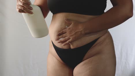 overweight adult hispanic woman in underwear applies moisturizing cream to her sagging abdomen