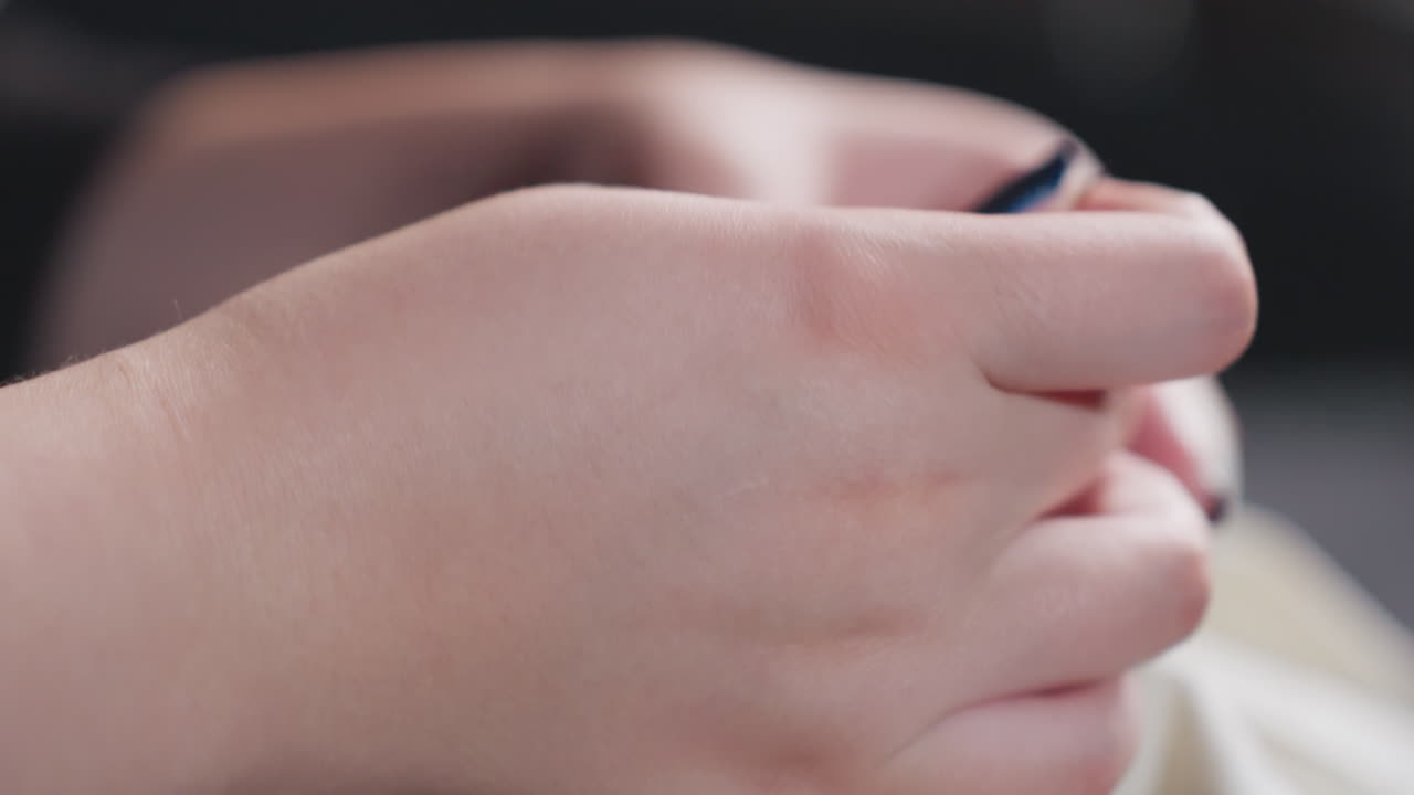 Close up of manicured hands stitching torn white dress with needle and thread, steady work on lap, black outfit, soft indoor light, focused repair of fabric seam captured in calm home setting