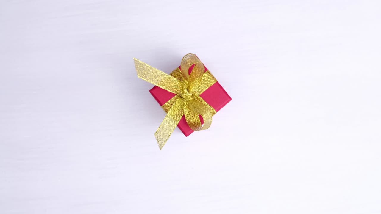 caja de regalo roja con cinta dorada girando sobre fondo de madera rosada. rotación de 360 grados. bucle sin costuras. ventas de concepto, precio de descuento, vacaciones de navidad y compras