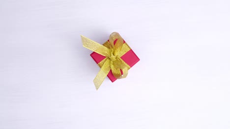 geschenkkiste rot mit goldenem band, das auf rosa holzhintergrund dreht. 360 grad drehung. nahtlose schleife. konzeptverkäufe, rabattpreis, weihnachtsferien und einkaufen