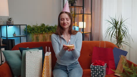 Happy-redhead-woman-celebrating-birthday-party,-makes-wish-blowing-burning-candle-on-small-cupcake