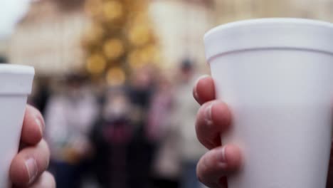 plastic cups with hot wine clinking in front of christmas tree, extreme closeup view