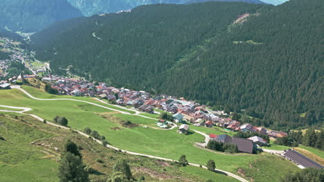 Drone-video-flying-towards-Dolomites-mountain-range-in-summer-flying-slowly-panning-up-over-historical-hillside-town-surrounded-by-forests-and-farmland