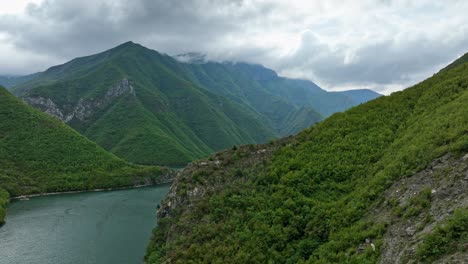 aerial ascend navigates to showcase the deep waters of lake koman, albania, between steep mountain cliffs on an overcast day