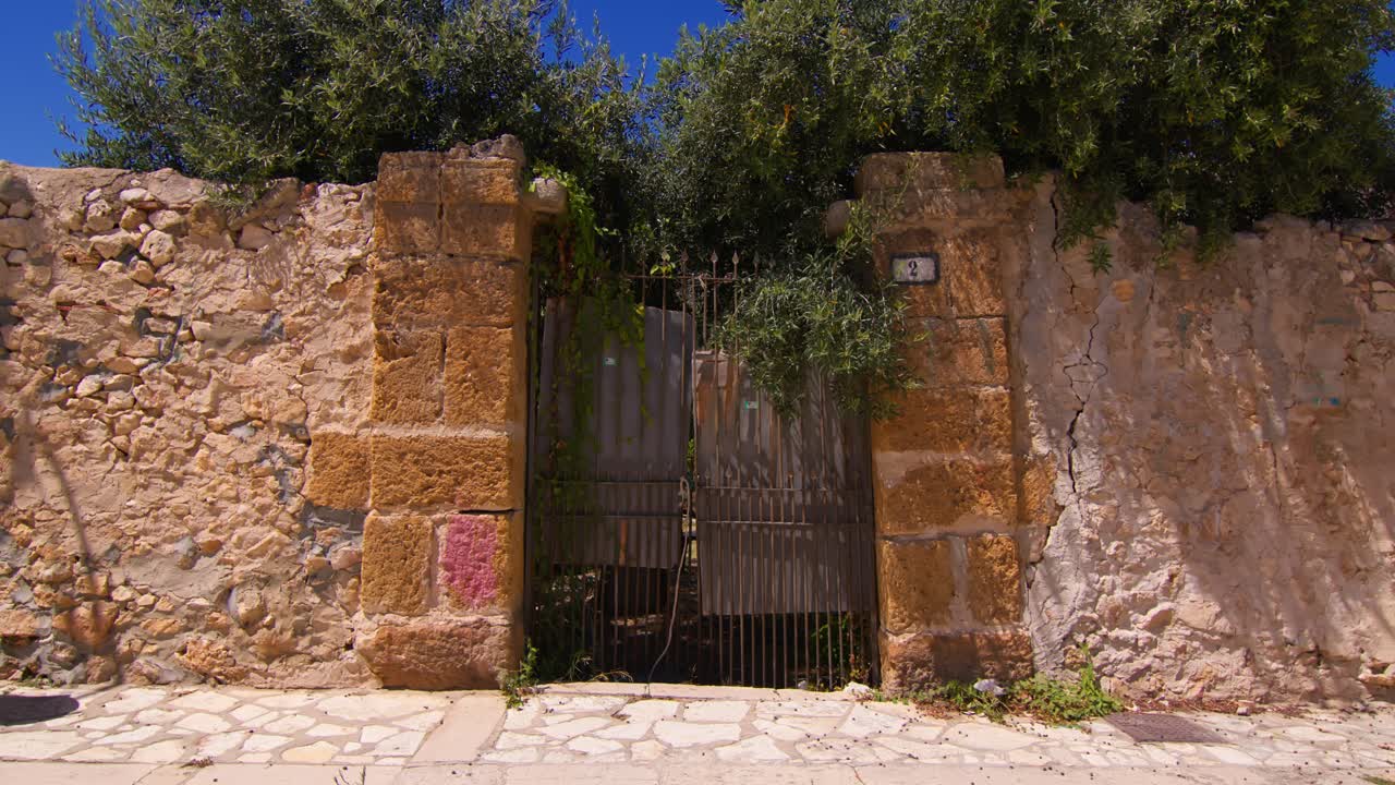 Old stone wall with gate in sunny Scopello city center, Sicilia, Italy