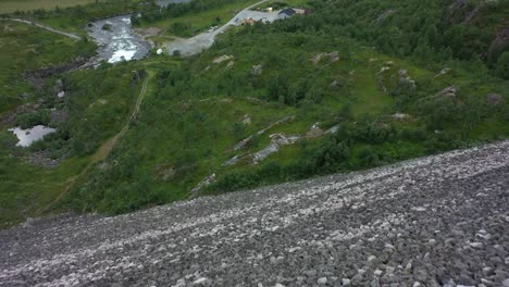 Flying-over-edge-of-massive-Sysen-dam-at-Hardangervidda-national-park-Norway---Rocky-landfill-embankment-to-store-water-for-hydroelectric-powerplant---Aerial-looking-down-from-edge