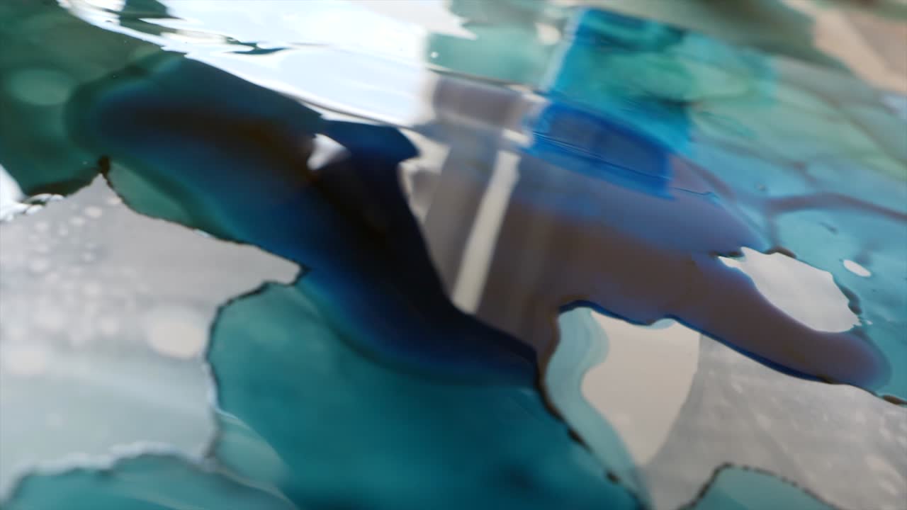 Artist hand pours liquid blue tint on sheet surface. Slow-motion